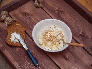 Breakfast of milk rice porridge and two toasts with cream cheese on a wooden rustic tray.