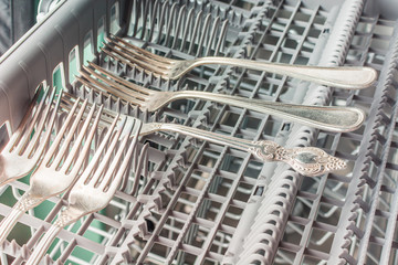 Silver forks lie in the upper compartment of the dishwasher