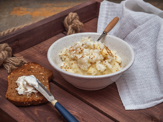 Freshly prepared milk rice porridge, in a deep plate a spoon with a wooden handle, toasts with cream cheese on a rustic wooden tray, a white cotton napkin.