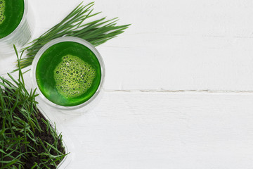 Wheatgrass fresh juice and  green wheatgrass plants isolated on white wooden background, copy space on the right side 
