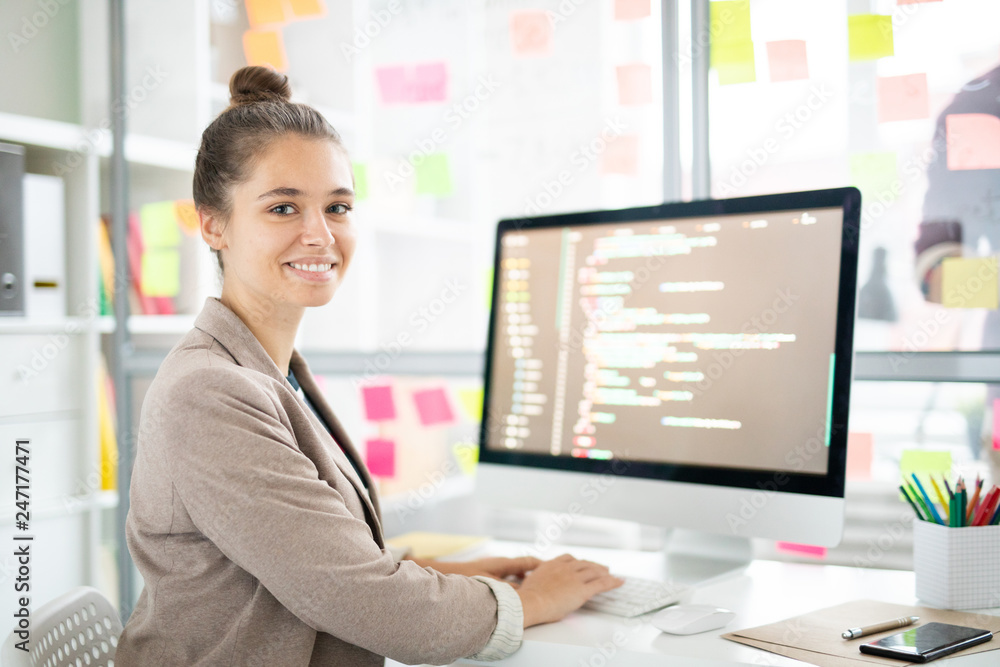 Leinwandbilder young casual woman sitting by desk in front of camera and analyzing coded data on computer screen