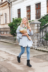 Young beautiful blonde woman in blue coat with bouquet of white tulips flowers walking outdoors on...