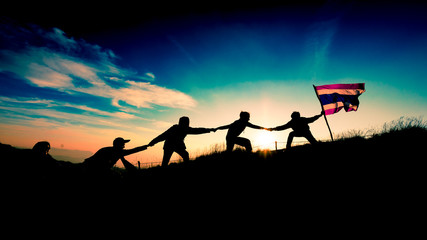 Leader handing Thailand Flag and climbers help A Team to conquer the summit in teamwork in a fantastic mountain landscape at sunset. Helping hand concept and international day of peace and teamwork.