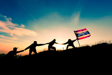Leader handing Thailand Flag and climbers help A Team to conquer the summit in teamwork in a fantastic mountain landscape at sunset. Helping hand concept and international day of peace and teamwork.