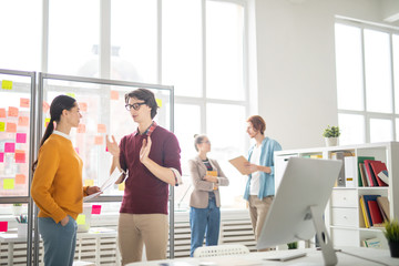 Two young economists in casualwear discussing creative ideas for project with their colleagues on...