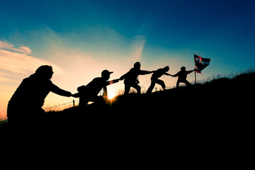 Leader handing Thailand Flag and climbers help A Team to conquer the summit in teamwork in a fantastic mountain landscape at sunset. Helping hand concept and international day of peace and teamwork.