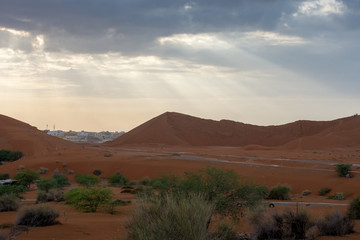 Fototapeta na wymiar Sun rays pierce the stormy clouds above the sand dunes in the UAE.