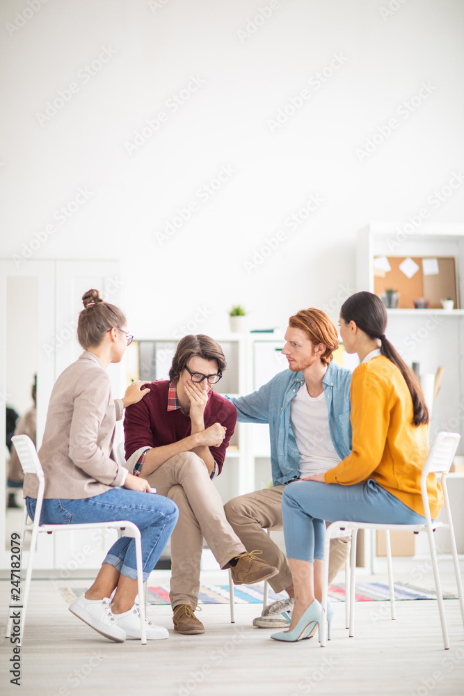 Wall mural desperate guy crying while sharing his trouble with groupmates while one of them supporting him duri