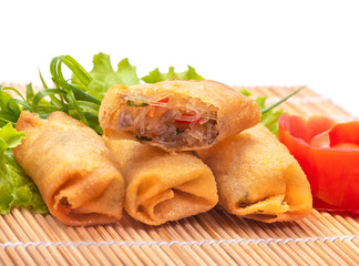 Spring rolls on bamboo mats with fresh vegetables on a white background
