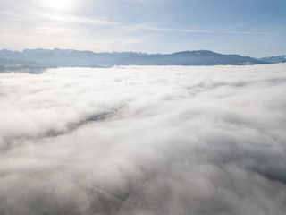 Aerial view of rural landscape in Switzerland covered with fog. Cold morning in winter with beautiful light. View from above the clouds with impressive sunlight.