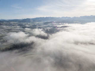 Aerial view of rural landscape in Switzerland covered with fog. Cold morning in winter with beautiful light. View from above the clouds with impressive sunlight.
