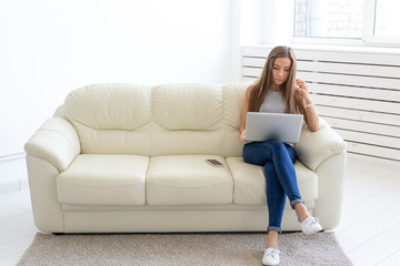 Freelance and people concept - Young woman sitting on a sofa and working at laptop