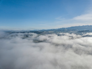 Aerial view of rural landscape in Switzerland covered with fog. Cold morning in winter with beautiful light. View from above the clouds with impressive sunlight.