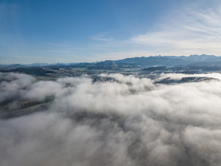 Aerial view of rural landscape in Switzerland covered with fog. Cold morning in winter with beautiful light. View from above the clouds with impressive sunlight.