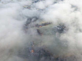 Naklejka premium Aerial view of rural landscape in Switzerland covered with fog. Cold morning in winter with beautiful light. View from above the clouds with impressive sunlight.