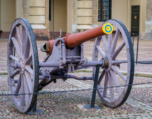ancient, historic gun in purple with a reddish-brown barrel, placed on a stone pavement