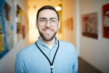 Head and shoulders portrait of smiling bearded man looking at camera while posing in art gallery, copy space