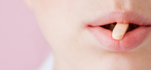 pink tablet in the mouth of the woman, close-up face