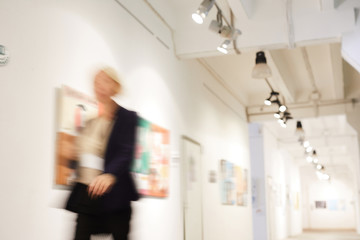 Blurred shape of unrecognizable woman walking in art gallery hall, copy space