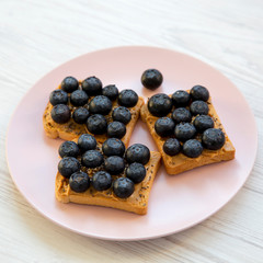 Fototapeta premium Vegetarian toasts with peanut butter, blueberries and chia seeds on a pink plate over white wooden surface, side view. Healthy eating and dieting.