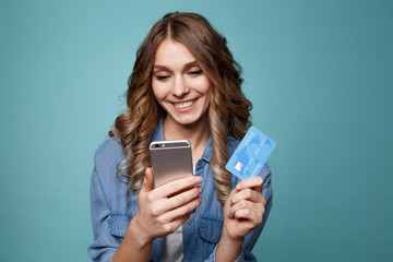 Fototapeta premium Image of excited young lady isolated over blue background using mobile phone holding credit card.