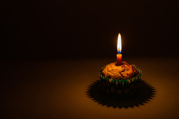 Banana chocolate chip muffin with birthday candle on dark background, with shallow depth of field.