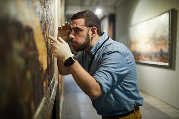 Side view waist up portrait of bearded museum worker inspecting painting for restoration, copy space