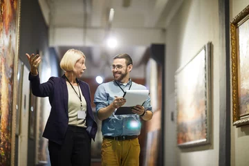 Foto op Aluminium Portrait of two cheerful museum workers discussing paintings walking in art gallery, copy space © Seventyfour