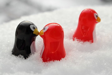 Love triangle or being third wheel. Having affair, infidelity or cheating concept. Unrequited love concept. Valentine's day concept. Three toy penguins in the snow. Focus is on the couple.