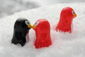 Love triangle or being third wheel. Having affair, infidelity or cheating concept. Unrequited love concept. Valentine's day concept. Three toy penguins in the snow. Focus is on the single one.
