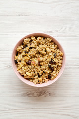 Fruit granola in pink bowl over white wooden background, top view. Flat lay, from above, overhead.