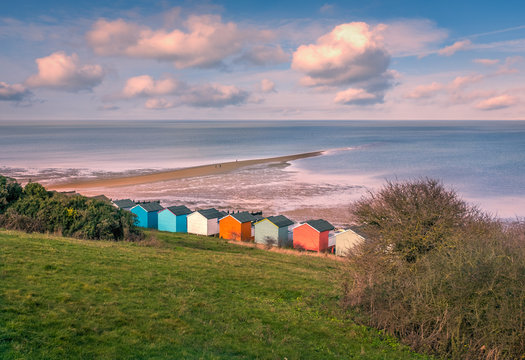 Impressive winter clouds in a cool blue sky over the beach huts and natural spit of land that stretches out to sea on the beach in Tankerton, Whitstable, Kent, UK.