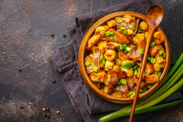 Spanish migas with pork and green onion in wooden bowl on dark background.