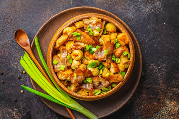 Spanish migas with pork and green onion in wooden bowl on dark background.