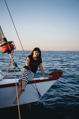 Obraz premium Young pretty woman in black shirt and striped skirt at luxury yacht in sea, sunset