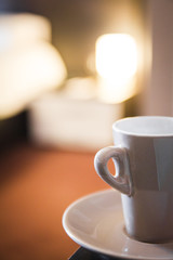 white mug of coffee on saucer in hotel room warm evening light