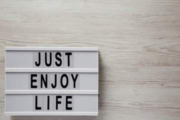 Modern board with text 'Just enjoy life' on a white wooden surface, top view. Space for text.