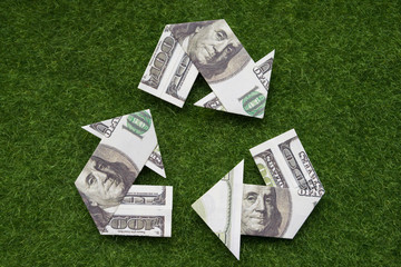 Triangular recycling symbol of dollar bills on green grass background. ecology. waste. profit.