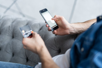 Online payment. Man's hands holding a credit card and using smart phone for online shopping.
