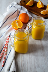 Fresh orange juice in glass jars over white wooden surface, low angle view. Close-up.