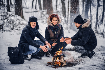 A group of happy friends staged a camping in the midst of a snowy forest, sitting around a campfire...