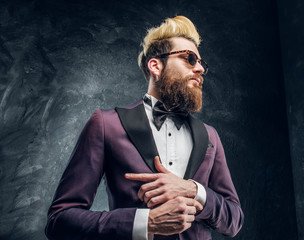 A young bearded man in sunglasses with expressive style dressed in a violet elegant suit standing...