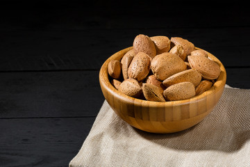 Almonds with shell in wooden bowls on slate background