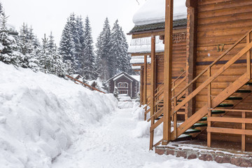 Fototapeta premium Chalet in the ski resort. Wooden house in the resort Bukovel in Ukraine. Two-storey cottages of logs. Natural building materials. Winter country landscape. Snow-covered houses. Wooden facade.