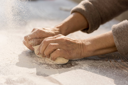 Hands of mature female kneading dough in flour on wooden table before making homemade pastry