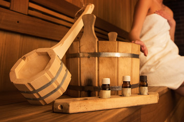Wooden bath accessories with aromatic oil bottle for bath in the sauna and woman on background