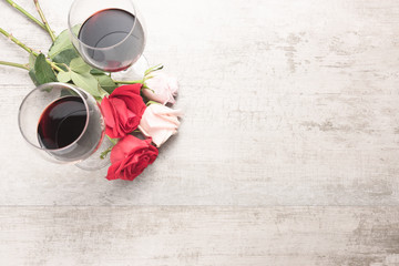 Top down view of two glasses of red wine with red and pink roses on a reclaimed wood surface.