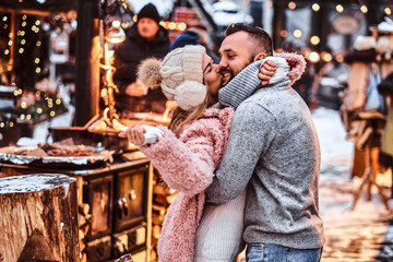 Obraz premium A cheerful attractive couple in love, enjoying spending time together while embracing at the winter fair at a Christmas time