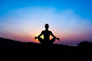 Silhouette of a young woman doing yoga on the beach at sunset.