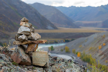 Stones stacked slide on top of each other in a tourist picturesque mountain range in the valley with the turquoise river, autumn